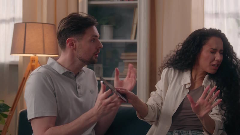 Couple arguing on the couch, with one partner trying to talk while the other pulls away during a repeated conflict